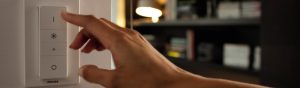 "Đang điều chỉnh công tắc điều chỉnh độ sáng đèn LED thông minh Philips, điều khiển ánh sáng môi trường trong phòng khách ấm cúng có giá sách."